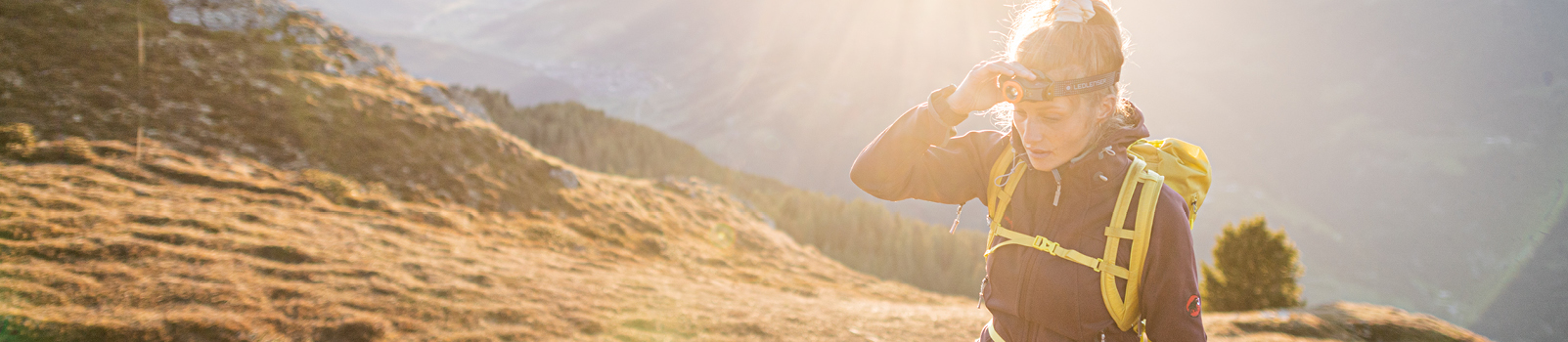 นักเดินป่าหญิงสวมไฟฉายคาดหัว Ledlenser บนเส้นทางภูเขายามแสงทอง (Female hiker wearing a Ledlenser headlamp on an alpine trail at golden hour)