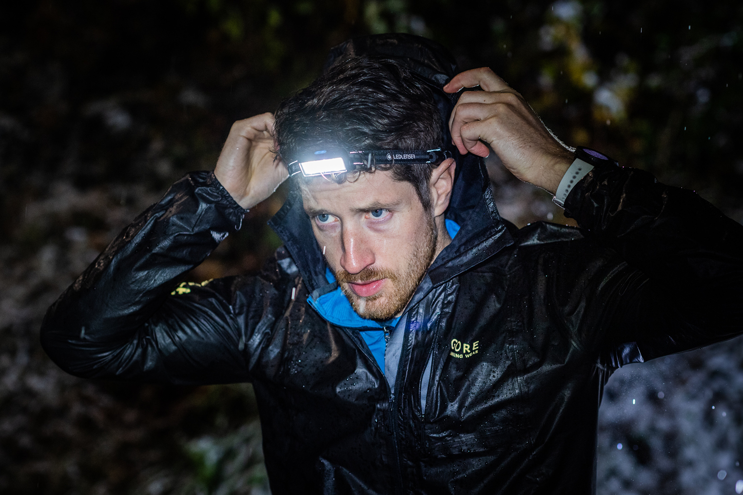 นักวิ่งเทรลใส่ไฟฉายคาดหัว Ledlenser วิ่งกลางคืนท่ามกลางสายฝน (Trail runner wearing a Ledlenser headlamp in the rain at night)