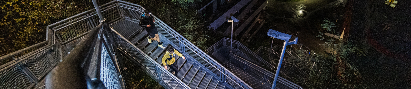 นักวิ่งสองคนสวมไฟฉายคาดหัว Ledlenser วิ่งขึ้นบันไดกลางคืน (Two runners wearing lit Ledlenser headlamps climbing stairs at night)