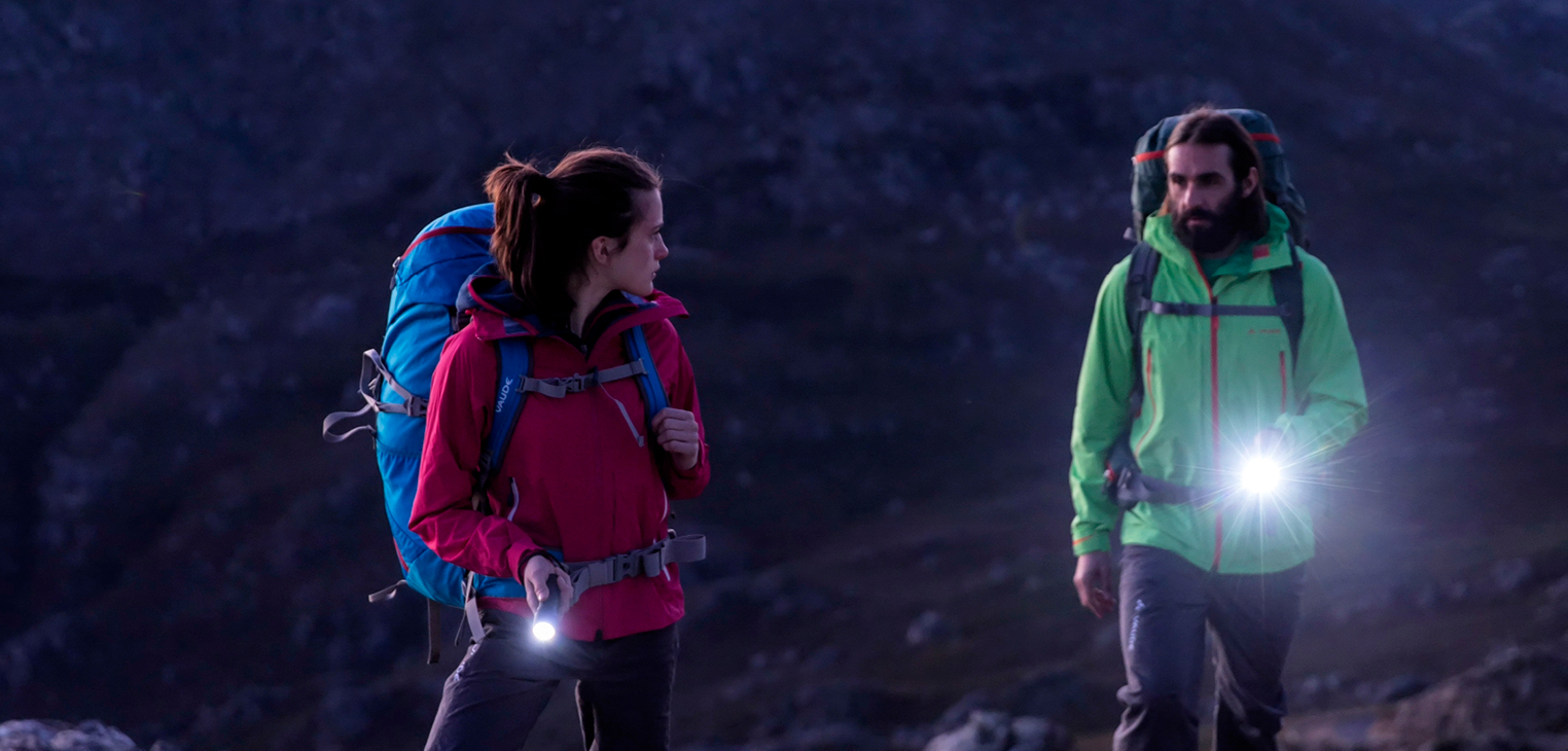 นักเดินป่าสองคนถือไฟฉายมือขณะเดินป่ากลางคืน (Two hikers using handheld flashlights on a night hike)