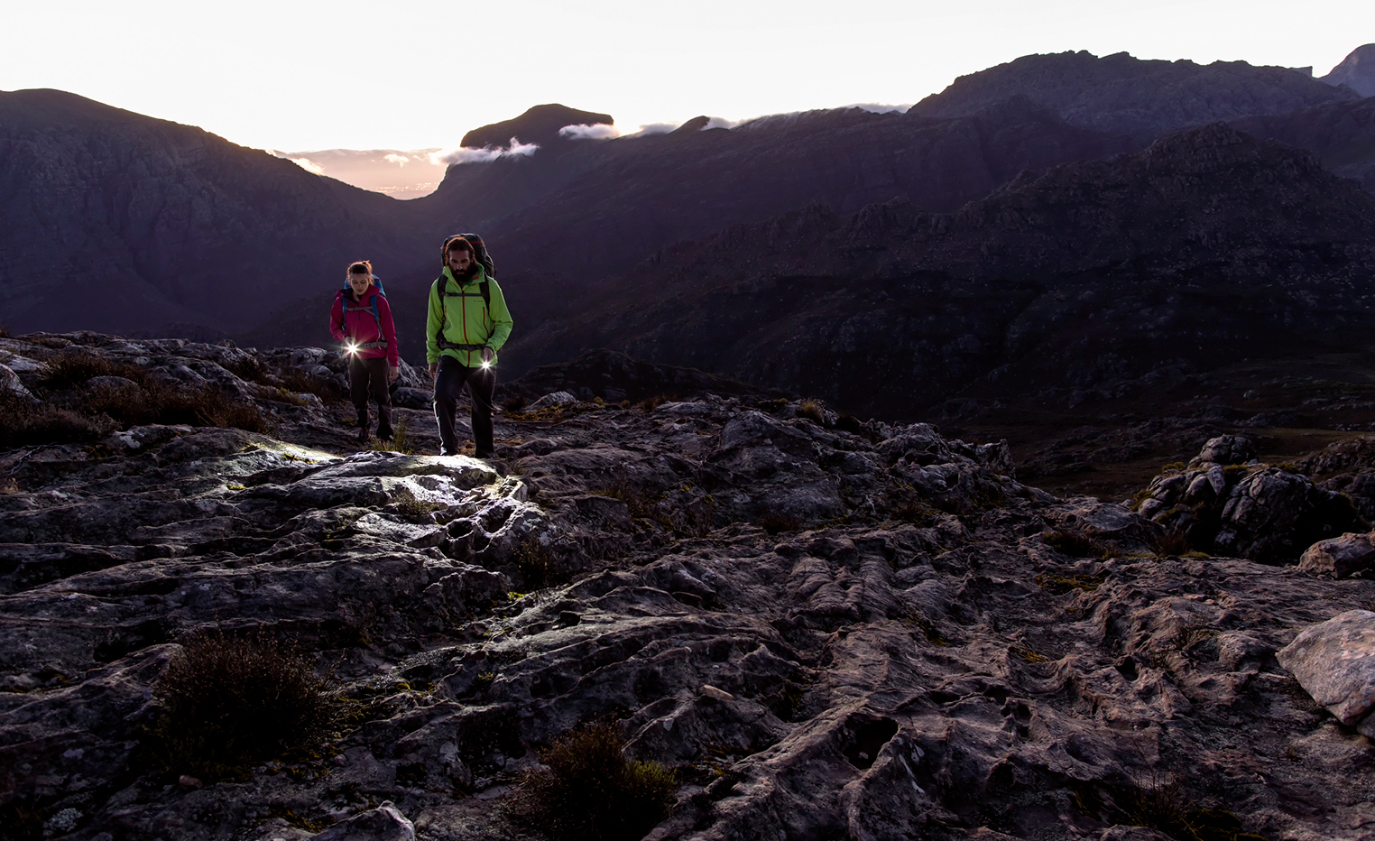 นักเดินป่าใช้ไฟส่องทางบนสันเขาหินยามเช้ามืด (Hikers lighting their way on a rocky ridge at dawn)